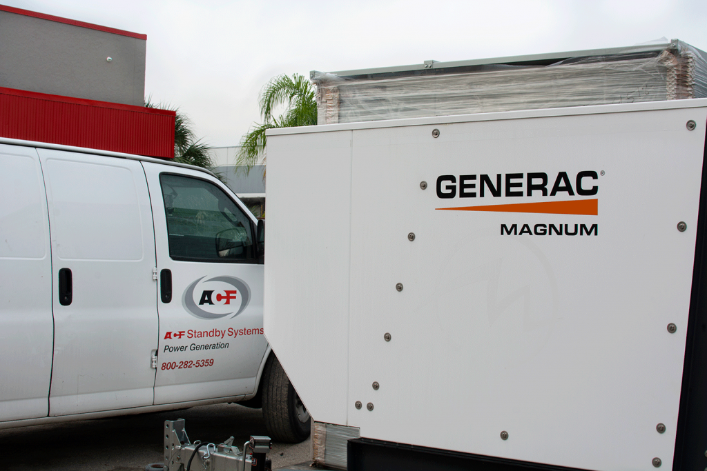 A white cargo van with Generac Magnum mobile generator unit branding parked next to a Generac Magnum mobile generator unit.